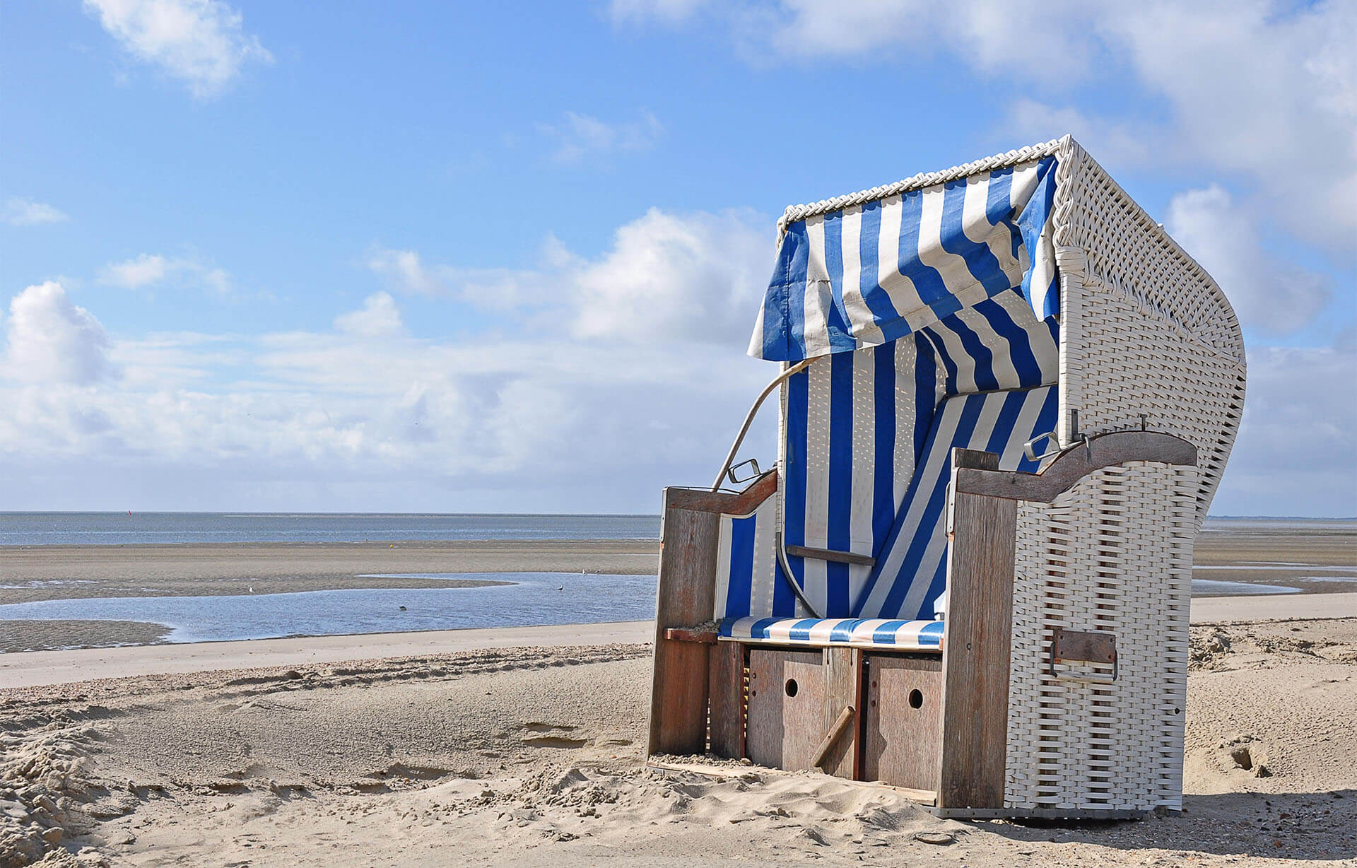 Ein einzelner Strandkorb steht am Nordseestrand, umgeben von feinem Sand, unter einem strahlend blauen Himmel bei schönem Wetter