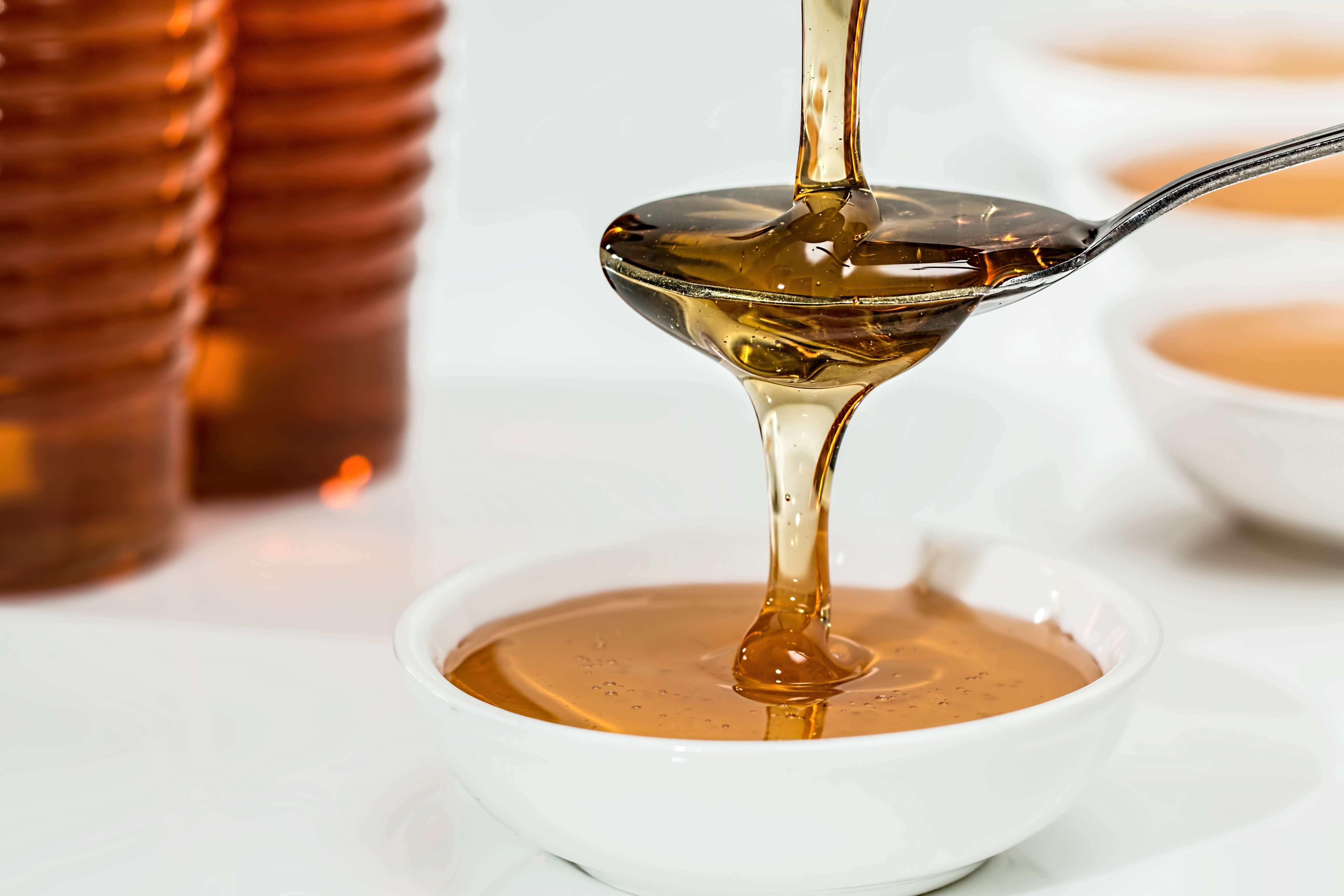 Flüssiger Honig und Sirup in Glasflaschen mit Ausgießer, dargestellt als alternative Süßmittel auf einem Holztisch.