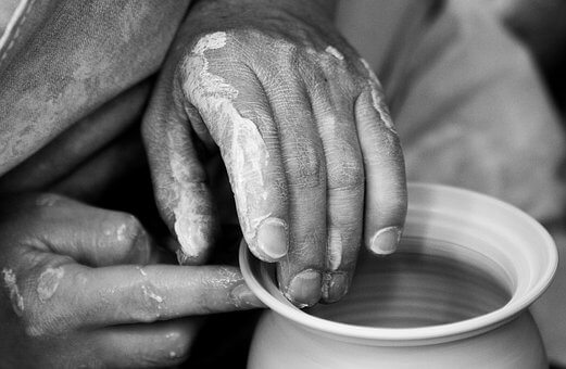 Schwarz-weiß Foto von mit Ton bedeckten Händen, die sorgfältig an einem Gefäß auf einer Töpferscheibe arbeiten, symbolisiert die Handwerkskunst in deutschen Manufakturen.