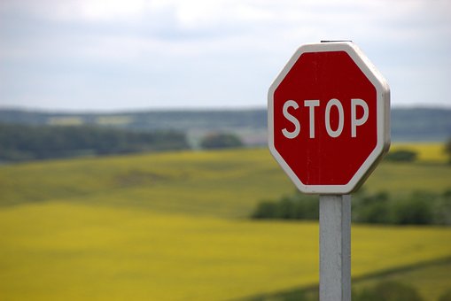 Ein Stop-Schild vor einem leuchtenden Rapsfeld, symbolisiert die Notwendigkeit, innezuhalten und die Bedeutung der Eigenfinanzierung zu reflektieren